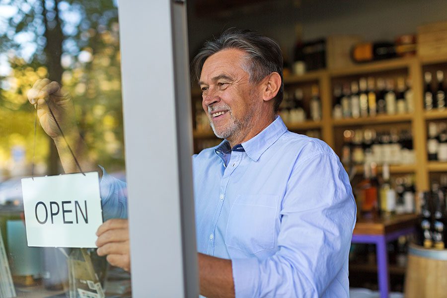 Business Insurance - Mature Wine Shop Owner Hanging Up Open Sign On Front Door